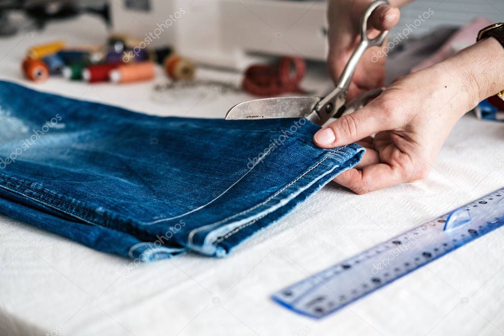 Tailor cutting jeans with scissors at workshop