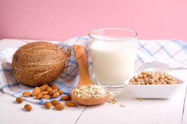 Alternatif tip Milks. Vegan yedek süt sütü. Süt cam, Hindistan cevizi, badem fıstığı, soya, pembe arka planda ahşap masada yulaf gevreği. Yiyecek ve içecek, sağlık, diyet ve beslenme konsepti