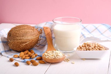 Alternative types of milks. Vegan substitute dairy milk. Milk glass, coconut, almond nuts, soy, oat flakes on wooden table on pink background. Food and drink, health care, diet and nutrition concept clipart