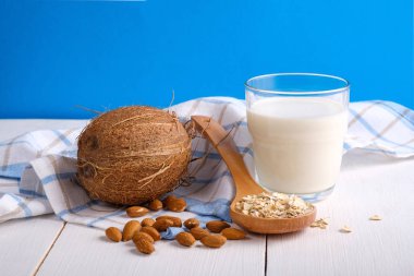 Alternatif tip Milks. Vegan yedek süt sütü. Mavi arka planda ahşap masada süt, Hindistan cevizi, badem fıstığı, yulaf gevreği bir bardak. Yiyecek ve içecek, sağlık, diyet ve beslenme konsepti