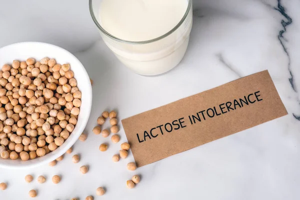 Lactose free milk concept. Homemade milk of nuts and piece of paper with text LACTOSE INTOLERANCE on marble background, non dairy milk from organic substitute, alternative milk type for vegan.