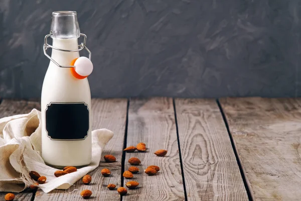 Bottle of vegan plant milk and almond nuts on wooden table on grey background. Banner with copy space. Dairy free milk substitute drinks and ingredients concept.