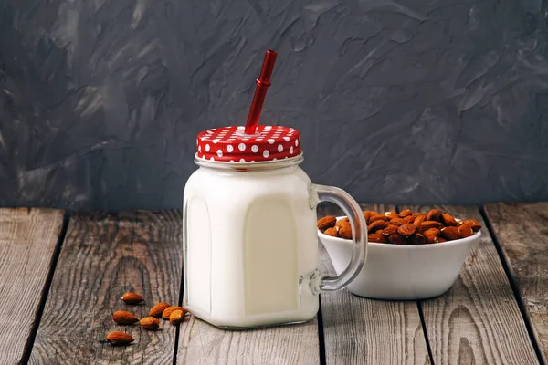 Cóctel de leche de almendras en frasco con nueces de almendras sobre mesa de madera sobre fondo gris. Comida alternativa vegana, concepto de alimentación limpia . — Foto de Stock