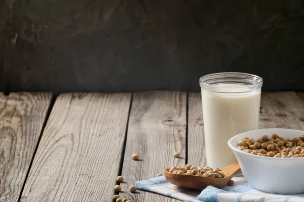 Leche de soja orgánica saludable alternativa libre de lácteos en taza y tazón con soja sobre fondo de madera oscura. Concepto de leche vegana sin lactosa . — Foto de Stock