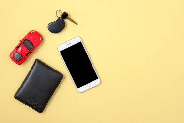 Online araç kiralama hizmeti konsepti. Kırmızı oyuncak araba, araç anahtarı, akıllı telefon, sarı arka planda otomatik sürücü lisansı. Üst görünüm. Online Mobil araç taşımacılığı sipariş için kullanım Smartphone