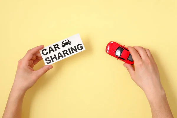Car sharing concept. Human hands holding red toy car model and text sign \