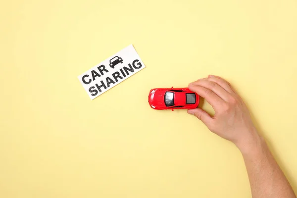 Car sharing concept. Human hand is driving red toy car model to text sign \