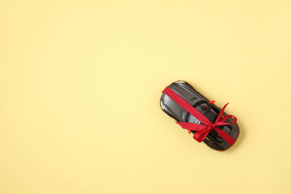 Car gift concept. Modern car with ribbon like a present on yellow background. Top view, flat lay composition.