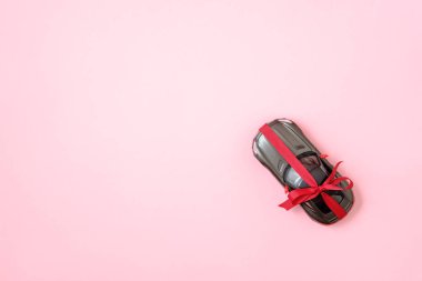 Bir hediye olarak kırmızı yay kurdele ile yeni modern araba. Pembe arka planda oyuncak araba hediye, düz bir kompozisyon yatıyordu. Üst görünüm