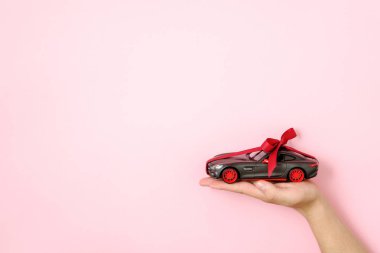 Oyuncak araba modeli kırmızı bir kurdele ile bağlı ve pembe arka planda insan eline yay. Otomatik Bayilik ve Kiralama, hediye veya mevcut olarak araba, araba çekmek, modern araba konsepti kazanmak için şans.