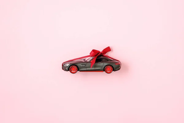 Modelo de coche de juguete con lazo de cinta sobre fondo rosa. Auto concesionario y alquiler, coche como regalo o presente, dibujar el coche, la oportunidad de ganar el concepto de coche moderno —  Fotos de Stock