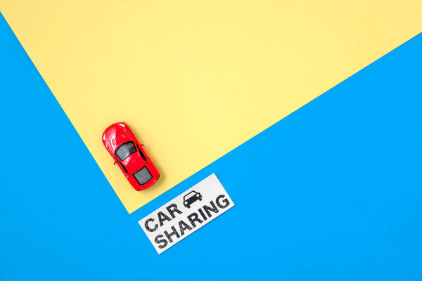 Car sharing concept. Red toy car model and text sign "CAR SHARING" on colorful blue and yellow background. Auto dealership and rental, sharing economy, taxi alternative, ridesharing