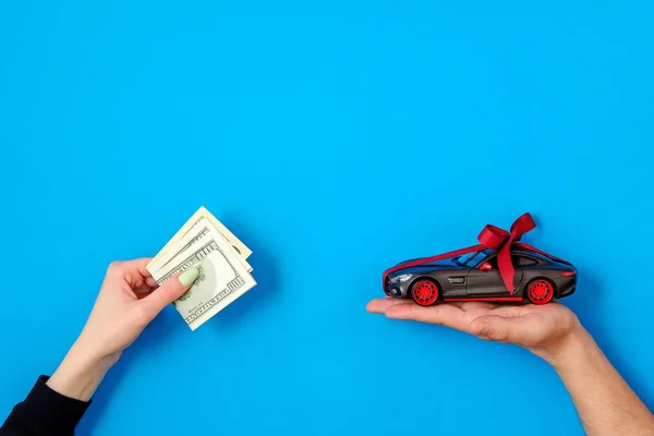Buy or rental car concept. The car dealer\'s hand make an exchange between the car and the customer\'s money. Salesman hand with toy car model with red ribbon and bow, customer hand with cash money