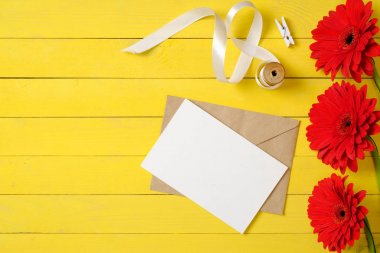 Boş kağıt kartı, pembe papatya çiçekleri, hediye kutusu ve sarı ahşap arka plan üzerinde etiketleri. Şık kadın masası. Yıldönümü konsepti. Üst te. Düz yatıyordu.