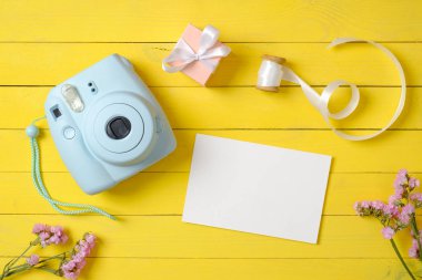 Modern anlık kamera, pembe çiçekler ve sarı ahşap arka plan üzerinde boş kağıt kart. Şık kadın masası. Yıldönümü konsepti. Üst te. Düz yatıyordu.