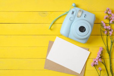 Modern anlık kamera, pembe çiçekler ve sarı ahşap arka plan üzerinde boş kağıt kart. Şık kadın masası. Yıldönümü konsepti. Üst te. Düz yatıyordu.