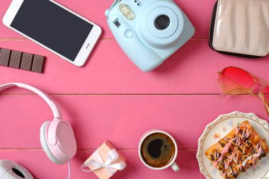Pembe ahşap arka plan düz yatıyordu kız aksesuarları. Anlık fotoğraf kamerası, akıllı telefon, kulaklık, hediye kutusu, kek, kahve fincanı, gözlük. En iyi kadın masası. Glamour kadın masa konsepti.