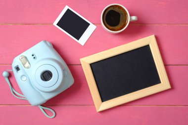 Düz yatıyordu, üstten görünümkadın masa masası. Anlık kamera, fotoğraf çerçevesi, anlık fotoğraf görüntüsü ve pembe ahşap arka plan üzerinde kahve fincan ı ile kadınsı masa çalışma alanı. Genç veya çekici kız Hobi.