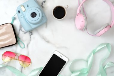 Şık aksesuarlar ve aletlerle dolu kadın masası. Modern fotoğraf makinesi, bir fincan kahve, cep telefonu, güneş gözlüğü, mermer arka planda kulaklık. Düz konum, üst görünüm. Bahar moda konsepti
