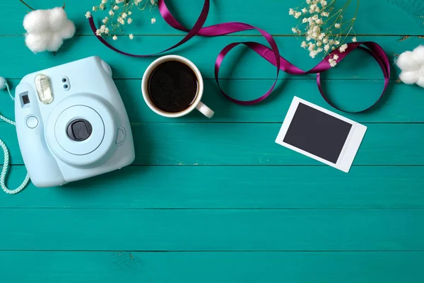 Modern instant camera, cup of coffee, instant photo image, tender flowers on green wooden background. Top view, minimal flat lay style composition. Women\'s desk, fashion blogger, beauty technology
