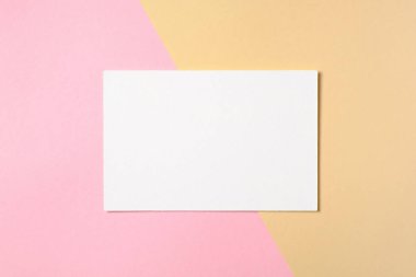 İki renkli pastel pembe ve sarı arka plan üzerinde boş beyaz kağıt kart. Düz yatıyordu, üstten bak, tepede. Yaratıcı düzeni, metin için boş alan ile tebrik kartı, afiş şablonu, güzellik günlüğü için mockup.