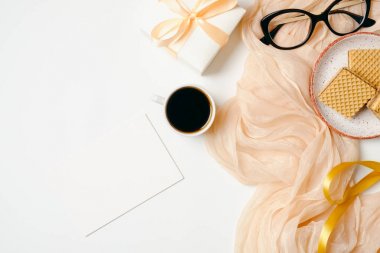 Boş kağıt kartı, eşarp, altın aksesuarlar, gözlük, kurdele, hediye kutusu, beyaz arka plan üzerinde kahve fincanı ile Kadın çalışma alanı. Düz güzellik blogger ev ofis masası yatıyordu. Üst görünüm kadınsı arka plan