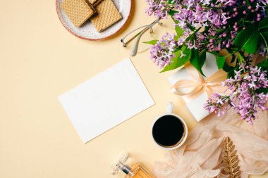 Sabah kahvesi, kağıt nota, waffle, leylak çiçeği, hediye kutusu, evde ki kadın masasında parfüm şişesi. Üst görünüm, ihale minimal düz döşeme tarzı kompozisyon. Moda blogger masaüstü. Kızlar kahvaltı konsepti