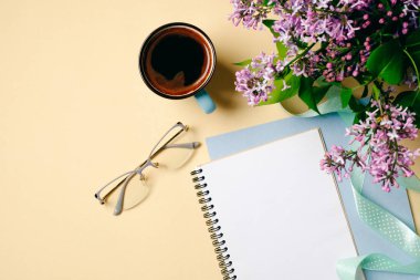 Düz yatıyordu ev ofis masası. Beyaz kağıt defter, gözlük, kahve fincanı ve bej arka planda leylak çiçekleri ile kadın çalışma alanı. Üst görünüm kadınsı arka plan. Moda blogger masaüstü konsepti.