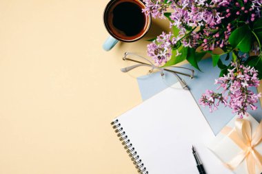 Düz yatıyordu ev ofis masası. Beyaz kağıt defter, gözlük, kahve fincanı ve bej arka planda leylak çiçekleri ile kadın çalışma alanı. Üst görünüm kadınsı arka plan. Moda blogger masaüstü konsepti.