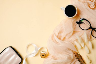 Kahve fincanı, bardaklar, ipek eşarp ve bej arka planda aksesuarları olan kadın ofis masası. Güzellik blogcusu çalışma alanı dümdüz uzanıyordu. Metnin için kopyalama alanı olan üst görünüm kadınsı arkaplan.
