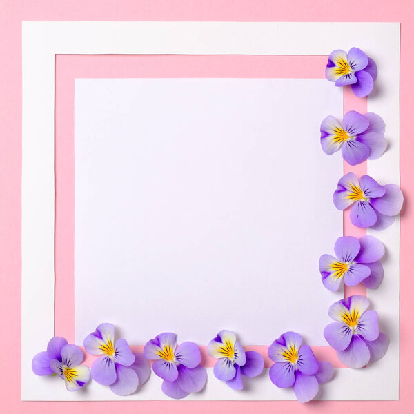 Creative flat lay composition: paper frame and blooming flowers petals on pink background. Top view, floral frame, abstract design. Invitation, greeting card or an element for your design