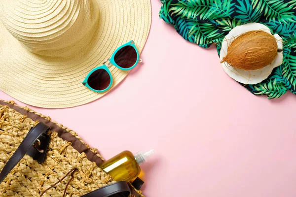 Women\'s beach accessories: straw hat, sunglasses, coconut, green scarf, beach bag with essential oil on pink background. Traveler stuff concept, summer background. Flat lay, top view, copy space.