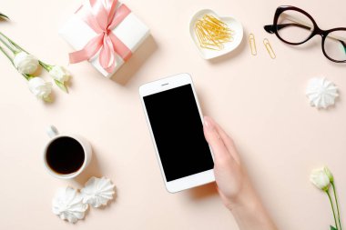 Düz yatıyordu ev ofis masası. Akıllı telefon, kahve fincanı, gözlük, çiçek, pembe arka plan üzerinde altın aksesuarlar tutan insan eli ile Kadın çalışma alanı. Üst görünüm kadınsı arka plan.