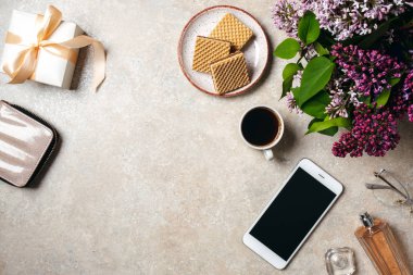 En iyi görünüm ev ofis masası çalışma alanı. Düz yatıyordu cüzdan, hediye kutusu, kahve fincanı, akıllı telefon, parfüm şişesi, gözlük, leylak çiçekler. Moda şeyler ile Kadınsı masa, güzellik blogger işyeri konsepti.
