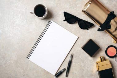 Beton taş arka plan üzerinde Düz yatıyordu kadınsı moda şeyler. Ev ofis masasında üst görünüm kadın aksesuarları. Boş kağıt defter, kalem, parfüm şişesi, altın çanta, güneş gözlüğü, kahve fincanı.