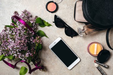Düz lila çiçekler, güneş gözlüğü, akıllı telefon, deri çanta, cüzdan, kadın kozmetik, beton arka plan üzerinde parfüm ile modern minimal ev çalışma masası yatıyordu. Üst görünüm kadınsı şeyler, moda blog kahraman