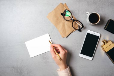 Düz boş kağıt kart, gözlük, kraft zarf, kahve fincanı, parfüm şişesi, akıllı telefon metin yazma kadın eli ile modern minimal ev çalışma alanı yatıyordu. Üst görünüm kadınsı masa, iş günlüğü kahraman