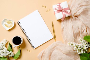 Düz yatıyordu kadınsı aksesuarlar, not defteri, ataş, altın kalem, hediye kutusu, kahve fincanı, pastel renkler arka plan üzerinde beyaz leylak çiçekler. Üst görünüm kadın masa kadın şeyler ile masa. Ev ofis konsepti