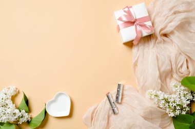 Düz yatıyordu kadınsı aksesuarlar, hediye kutusu, ruj, pastel renkler arka plan üzerinde beyaz leylak çiçekler. Kadın şeyler ile üst görünüm kadın masa masası.