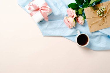 Düz yatıyordu hediye kutusu, kahve fincanı, gül çiçek buketi, kraft kağıt zarf ve kopya alanı ile pastel pembe arka plan üzerinde mavi tekstil bezi. Top view kadın masası, moda günlüğü kahraman afiş mockup.