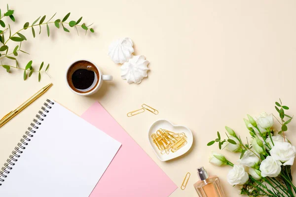 Flat lay home office desk, top view. Feminine accessories on pastel beige background. Coffee cup, paper notepad, golden paper clip, roses flower bouquet. Women home office desk, beauty blogger diary