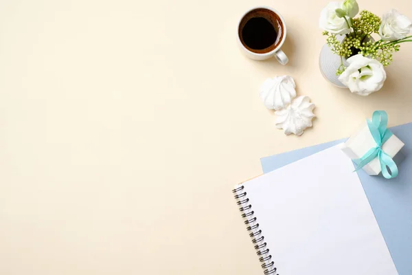 Frauen Home-Office-Schreibtisch mit leerem Papier Notizblock, Kaffeetasse, Geschenkbox, Blumenstrauß und femininen Modeaccessoires auf beige pastellfarbenem Hintergrund. flache Lage, Draufsicht, Kopierraum. — Stockfoto