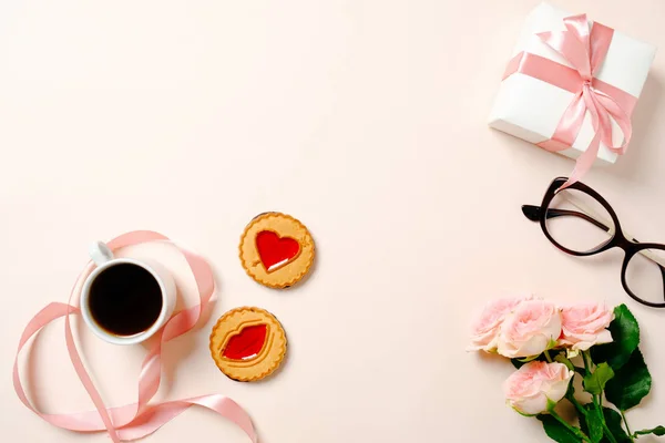 Επίπεδη θέση στο γραφείο του γραφείου. Γυναικείος χώρος εργασίας με κορδέλα, φλιτζάνι καφέ, κουτί δώρου, μπισκότα και τριαντάφυλλα λουλούδια σε ροζ φόντο. Γυναικείο φόντο κορυφαίας προβολής με χώρο αντιγραφής για κείμενο. — Φωτογραφία Αρχείου