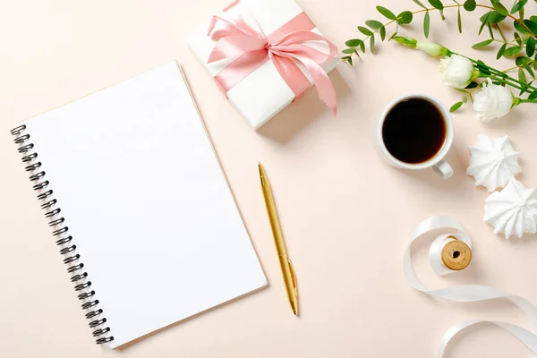 Wohnung lag Homeoffice Schreibtisch. Frauenarbeitsplatz mit leerem Notizbuch aus Papier, Kaffeetasse, Geschenkbox, Marshmallows und Rosenblüten auf rosa Hintergrund. femininer Hintergrund von oben mit Kopierraum für Text. — Stockfoto