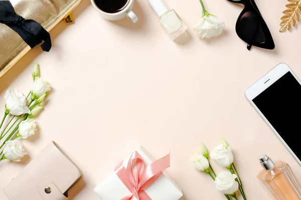 Espacio de trabajo femenino con smartphone, flores rosas, accesorios dorados, caja de regalo, vasos, taza de café. Escritorio de oficina de mujeres laicas planas. Vista superior fondo femenino . —  Fotos de Stock
