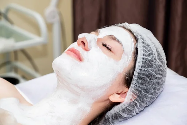 Face mask, spa beauty treatment. Young beautiful girl applying facial clay mask at spa salon, skin care concept.