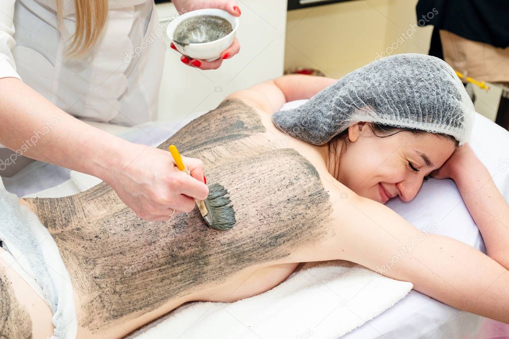Beautiful young girl having seaweed cosmetic mask and body massage with scrub in spa salon