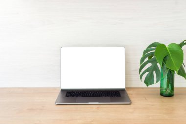 Boş ekran mockup ve ahşap yüzeyüzerinde monstera bitki ile dizüstü bilgisayar ile Ofis masası masa. Minimal stil işyeri konsepti.