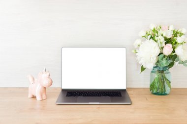 Boş beyaz ekranlı dizüstü bilgisayar, tek boynuzlu at, ofis işyerinde çiçek buketi. Kadınsı ev ofis masası. Şık çalışma alanı sahte.