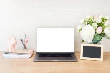 Boş beyaz ekran, sarf malzemeleri, resim çerçevesi, kadınsı aksesuarlar ve ahşap yüzeyüzerinde çiçek buketi ile dizüstü bilgisayar ile Ev ofis masası masa. Şık kadın işyeri konsepti.